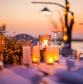 Cena romantica all'aperto con candele e tramonto sullo sfondo.