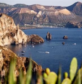 Vista panoramica delle isole Eolie con mare e barche, vegetazione in primo piano.