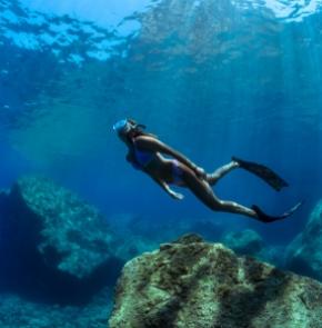 Subacquea esplora il fondale marino con pinne e maschera, circondata da rocce.