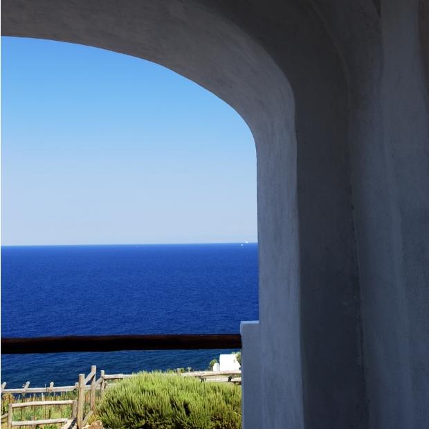 Vista sul mare attraverso un arco bianco, cielo azzurro e vegetazione.