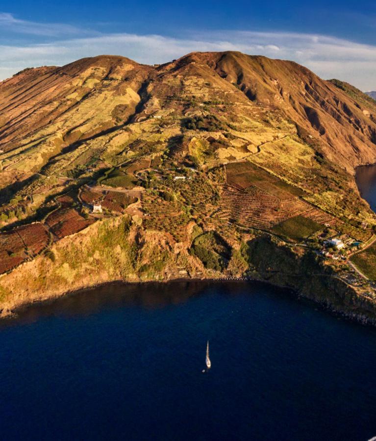 Isola vulcanica con coste rocciose e campi coltivati, circondata dal mare.