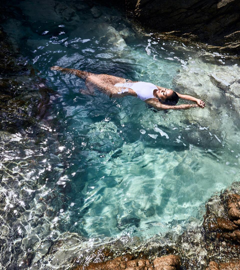 Persona in costume bianco galleggia in acque cristalline tra le rocce.